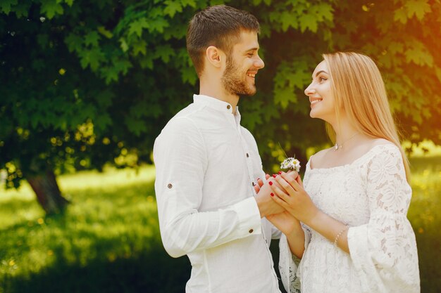 fille avec des cheveux clairs et une robe blanche marche dans une forêt ensoleillée avec son petit ami