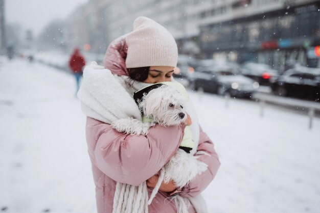 Fille avec un chien dans ses bras sur une rue de la ville la neige tombe