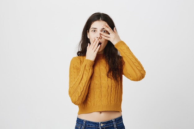 Fille choquée embarrassée regarde à travers les doigts, haletante