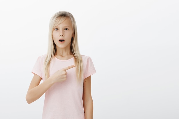 Fille choquée pointant vers la droite et la mâchoire tombante étonnée