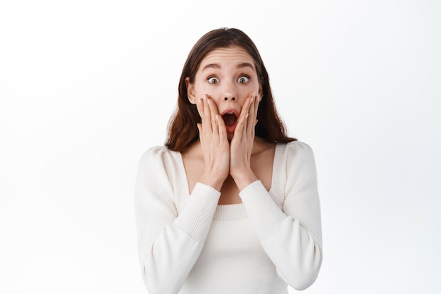 Une fille choquée se tenant la main près de la bouche ouverte, le regard fasciné par l'incrédulité face à une bonne nouvelle chanceuse, le regard étonné, gagnant et se réjouissant, haletant impressionné, fond blanc