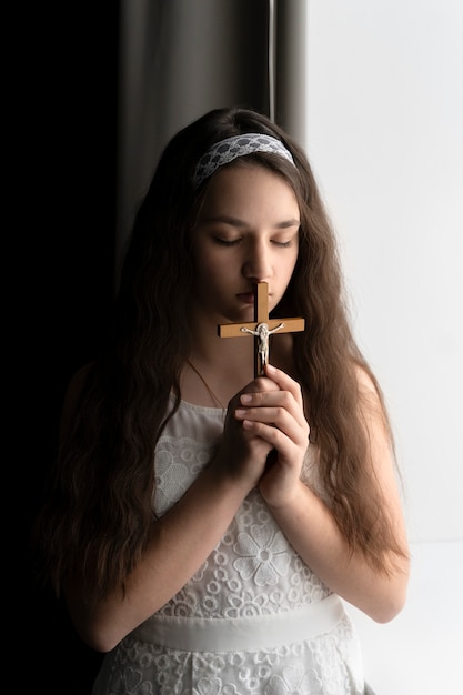 Fille chrétienne à coup moyen priant avec crucifix