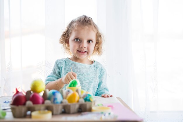 Fille à colorier les oeufs et regarder la caméra