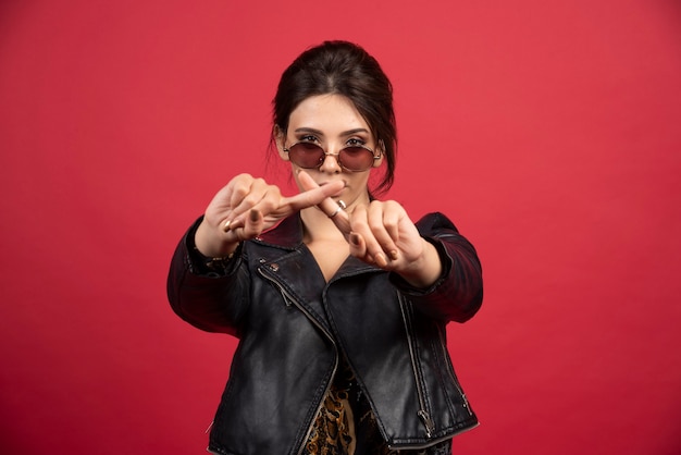 Fille cool en veste de cuir noir croisant les mains ou les doigts pour arrêter quelque chose.