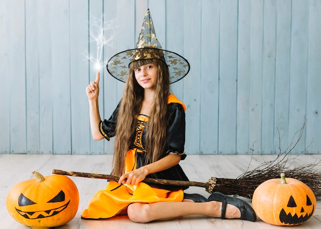 Fille en costume de sorcière assise sur le sol en train de faire de la magie