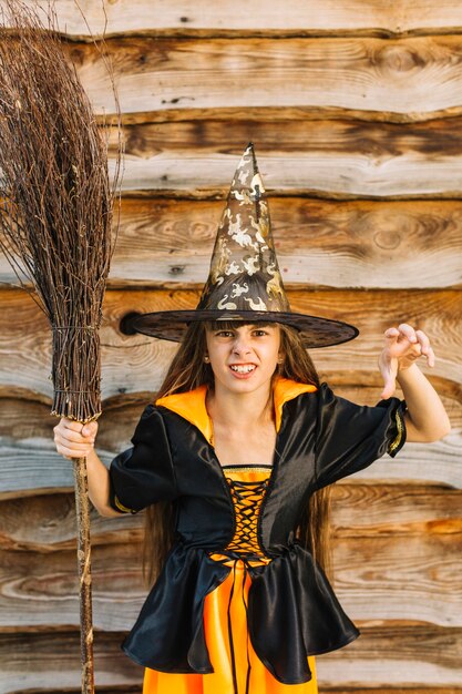 Fille en costume de sorcière montrant la main avec le balai