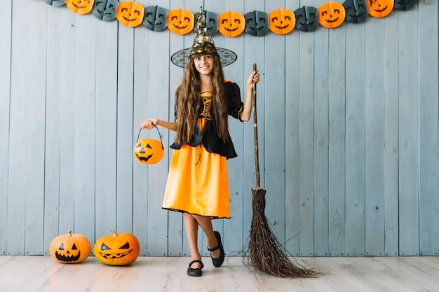 Fille en costume de sorcière tenant un panier d&#39;Halloween et un balai