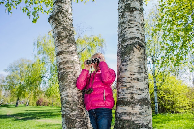 Une fille curieuse avec des jumelles dans le parc