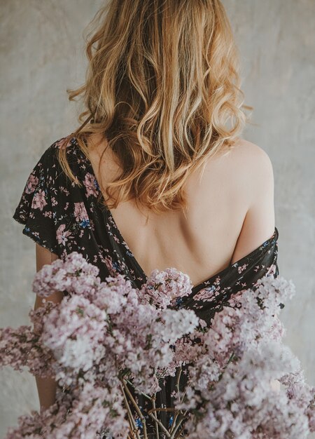 fille dans une robe avec un dos avec une épaule nue et un bouquet de lilas