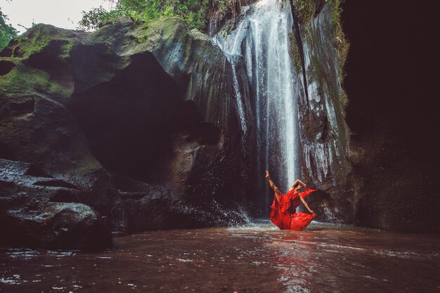 Fille dans une robe rouge dansant dans une cascade.