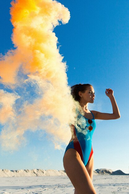 Fille en danse bleue avec une fumée orange sur la plage blanche