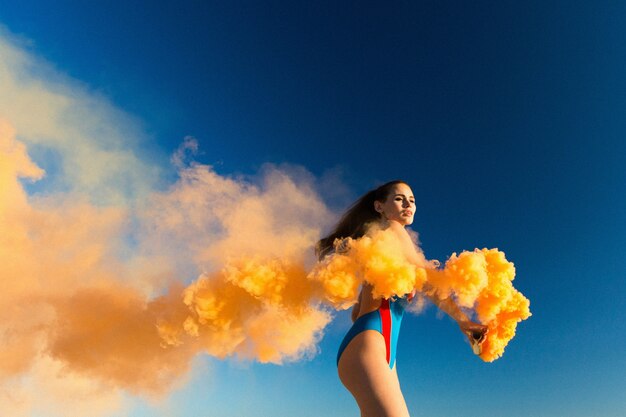 Fille en danse bleue avec une fumée orange sur la plage blanche