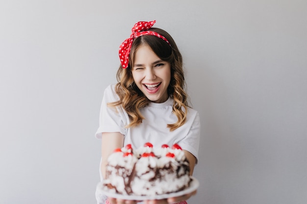 Fille Debonair avec une coiffure romantique posant avec un gâteau d'anniversaire. Incroyable dame qui rit tenant la tarte aux fraises.