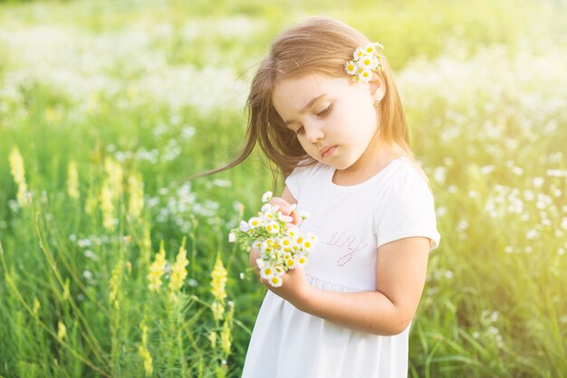 Fille debout dans le champ en regardant des fleurs blanches