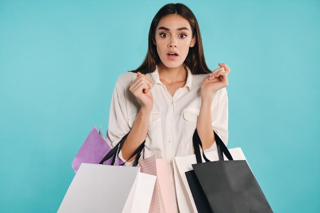 Fille décontractée choquée avec des sacs à provisions étonnamment regardant à huis clos sur fond coloré