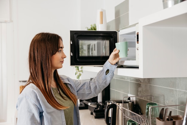 Fille décontractée utilisant un micro-ondes pour chauffer la tasse