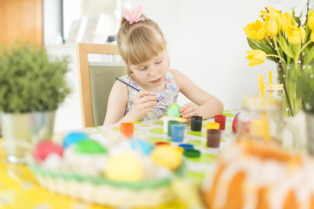 Fille décorer des oeufs de Pâques à table