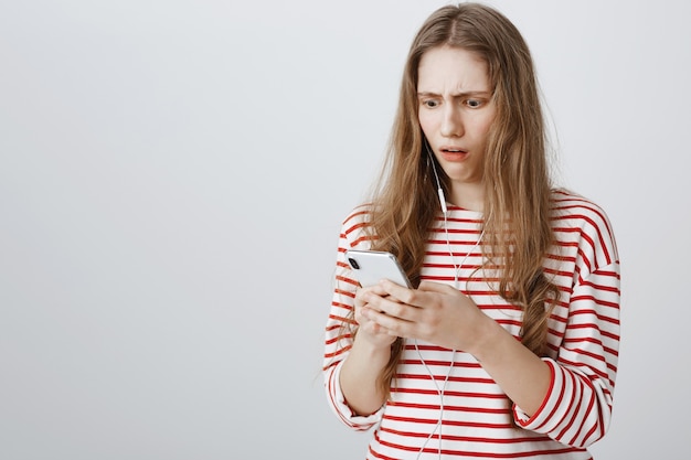 Une fille dégoûtée et surprise regarde l'écran du téléphone portable concerné