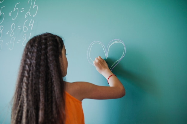 Fille dessinant le coeur sur le tableau