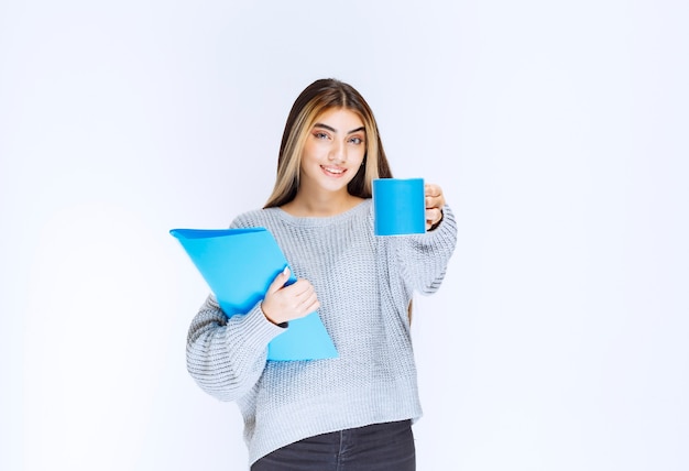 Fille avec un dossier bleu partageant une tasse de café avec son collègue.
