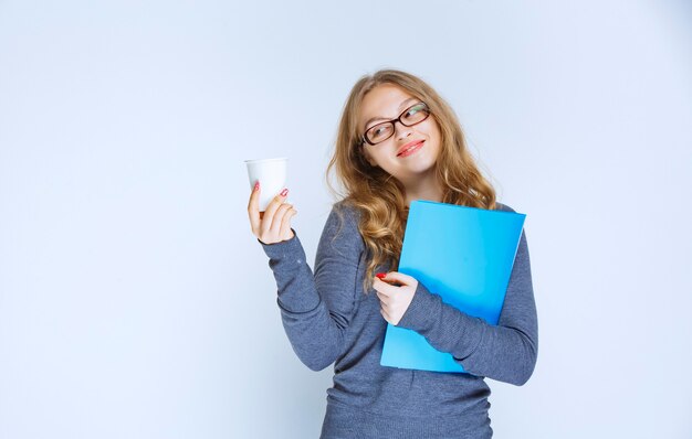 Fille avec un dossier bleu tenant une tasse de café jetable.