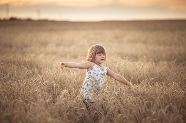 Une fille drôle danse dans un champ avec du seigle au coucher du soleil