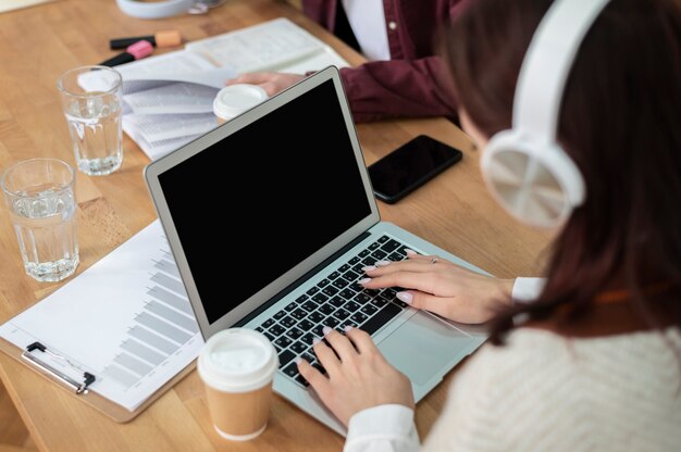 Fille avec des écouteurs utilisant un ordinateur portable avec ses camarades de classe pendant l'étude en groupe