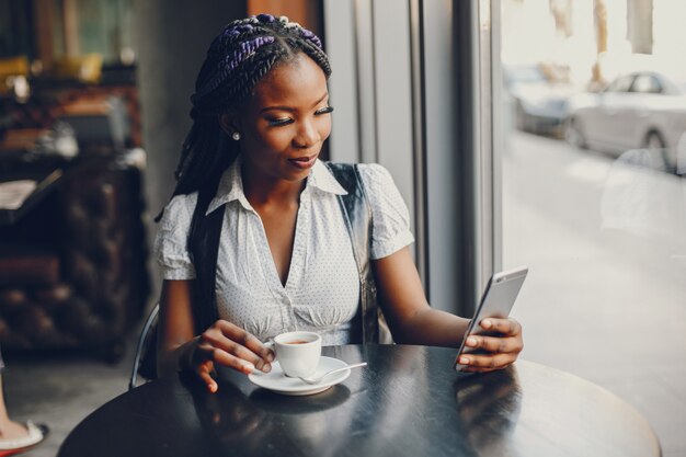 Une fille élégante et belle à la peau foncée est assise dans un café