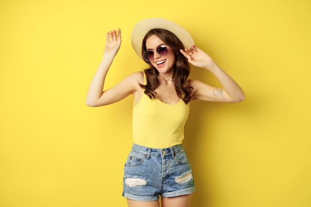 Fille élégante en chapeau de paille et débardeur prêt pour l'été partant en vacances et souriant debout heureux...