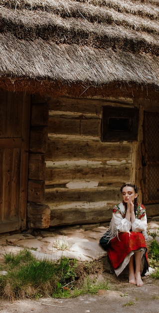 Fille élégante en costume traditionnel, assise à côté de la maison