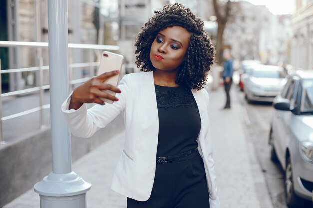 Fille élégante et élégante à la peau foncée avec des cheveux bouclés et dans une veste blanche debout