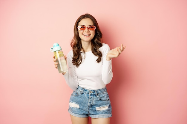 Fille élégante en tenue de printemps portant des lunettes de soleil tenant une bouteille d'eau avec une boisson saine au citron rire...