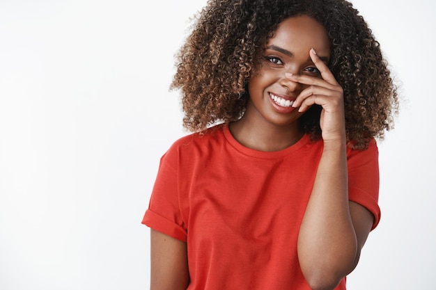 Fille entendant un compliment rougissant et regardant avec un regard affectueux sincère à la caméra tenant la main sur le visage timide et tendre souriant largement debout joyeux