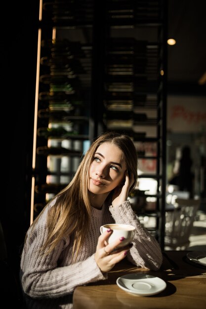 La fille est assise dans un café avec une tasse de café ou de thé. Photo avec des ombres