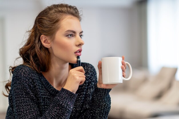 La fille est chez elle. Femme seule dans sa chambre. Elle est assise sur la table et écrit quelque chose dans son cahier à l'aide du crayon