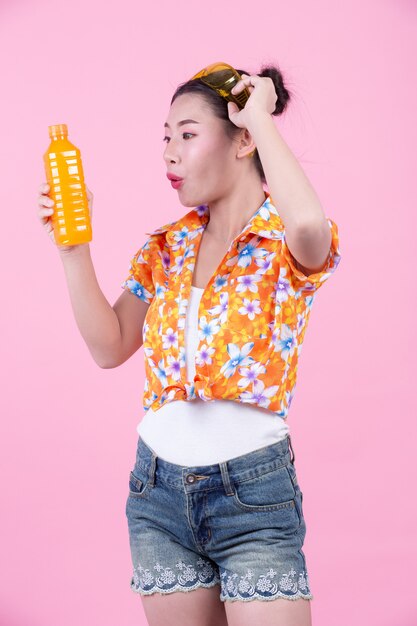 La fille est titulaire d&#39;une bouteille de jus d&#39;orange sur un fond rose.