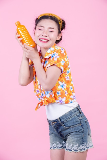 Photo gratuite la fille est titulaire d'une bouteille de jus d'orange sur un fond rose.