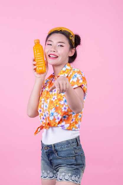 La fille est titulaire d&#39;une bouteille de jus d&#39;orange sur un fond rose.