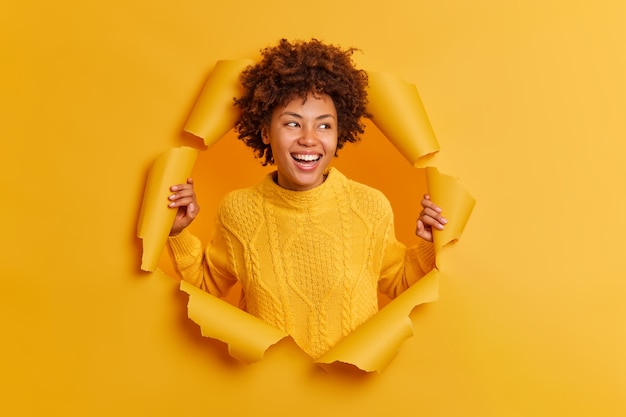 Une fille ethnique heureuse aux cheveux afro bouclés sourit largement concentrée sur le côté glousse positivement