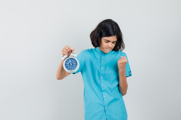 Fille étudiante en chemise bleue tenant horloge tout en montrant le geste du gagnant