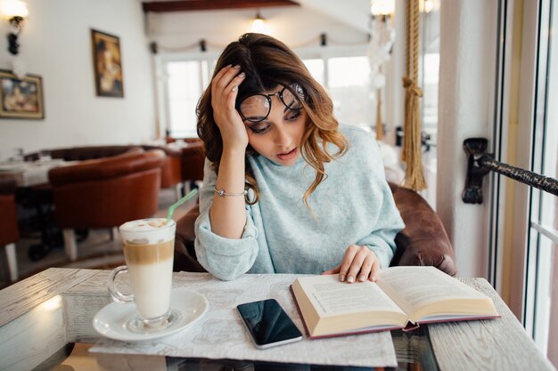 Fille étudiante fatiguée, lecture de la littérature scientifique au café