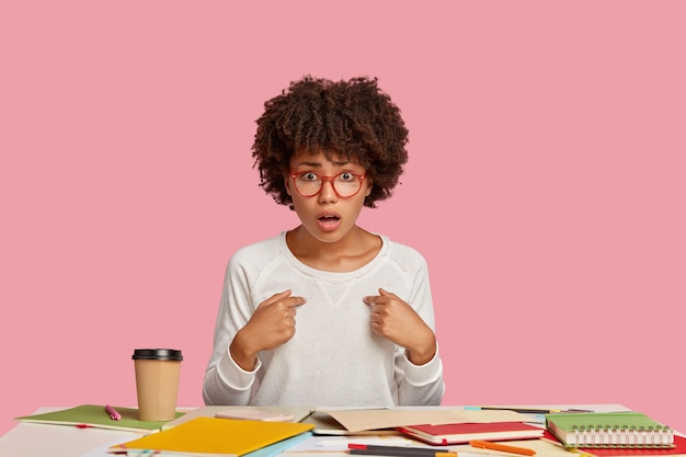 Photo gratuite fille étudiante indignée posant au bureau contre le mur rose