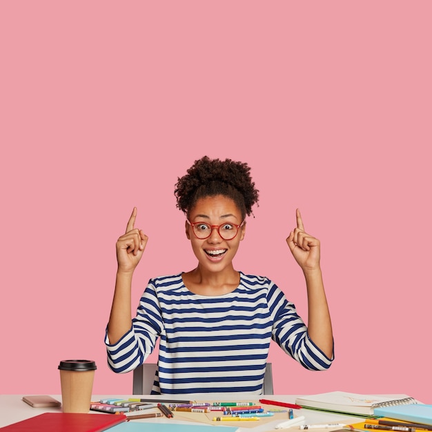 Photo gratuite fille étudiante ravie posant au bureau contre le mur rose