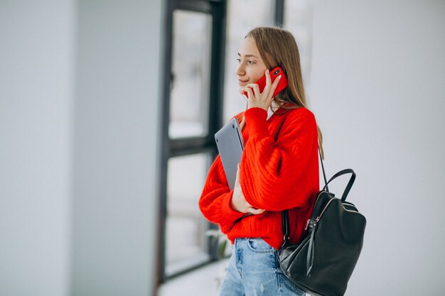 Fille étudiante tenant un ordinateur et parler au téléphone par la fenêtre