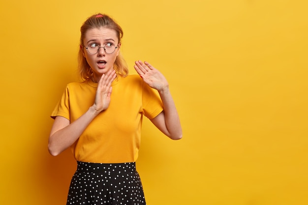 Une fille européenne effrayée et perplexe garde les paumes en avant et demande de ne pas s'approcher, dit de rester loin de moi à la recherche de quelque chose