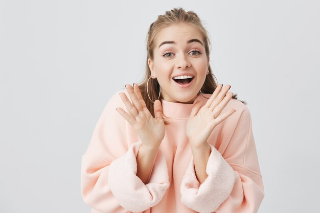 Fille européenne surprise avec les mains levées, étonnée ou choquée par des nouvelles inattendues, se tenant la main et montrant une expression heureuse. Jeune femme blonde montrant des émotions.