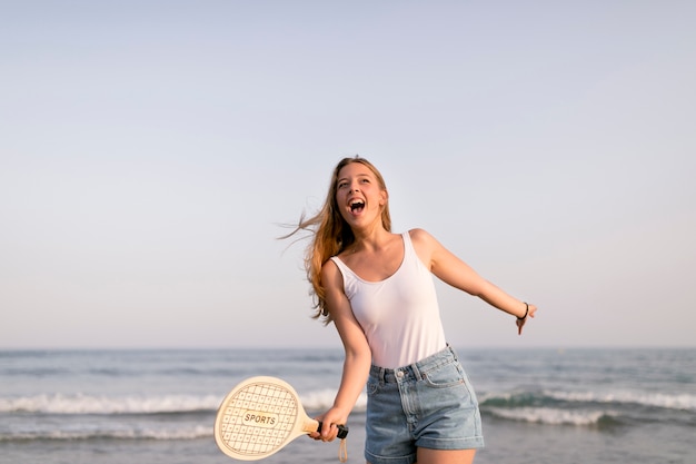 Photo gratuite fille excitée debout devant le bord de la mer en jouant au tennis