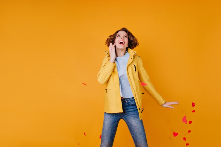 Photo gratuit fille excitée en jeans et manteau d'automne sautant et jetant des coeurs en papier. femme active romantique célébrant la saint-valentin en studio.