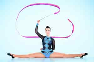 Photo gratuite la fille faisant de la gymnastique danse avec ruban de couleur sur un mur bleu