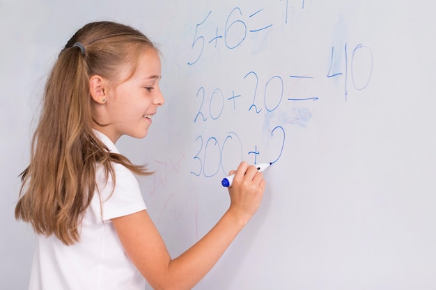 Fille faisant des maths sur un tableau blanc